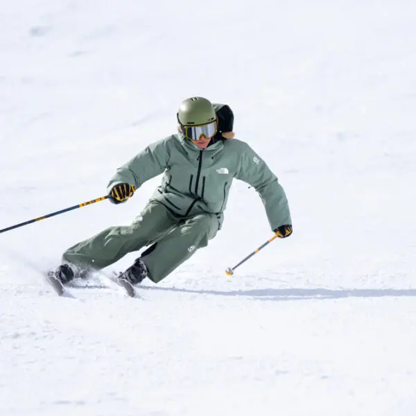 Skier in green jacket carving a sharp turn on groomed slope
