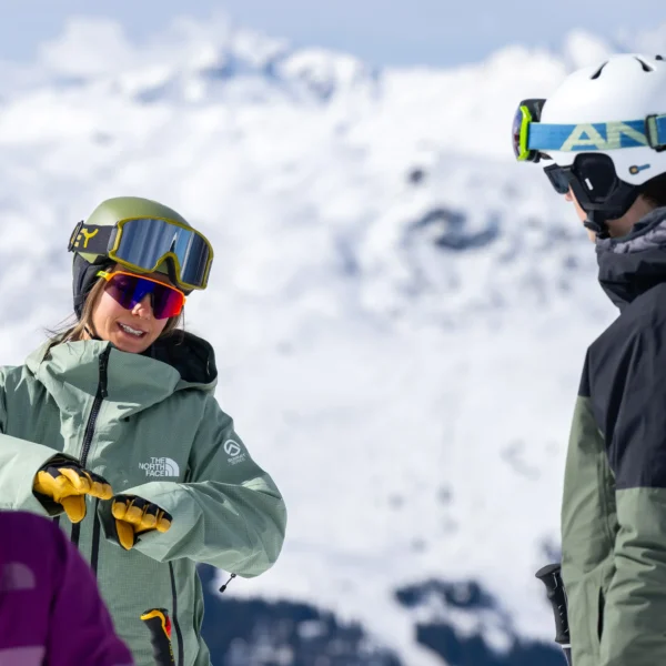 A ski instructor explaining a concept to a trainee ski instructor with a mountain backdrop