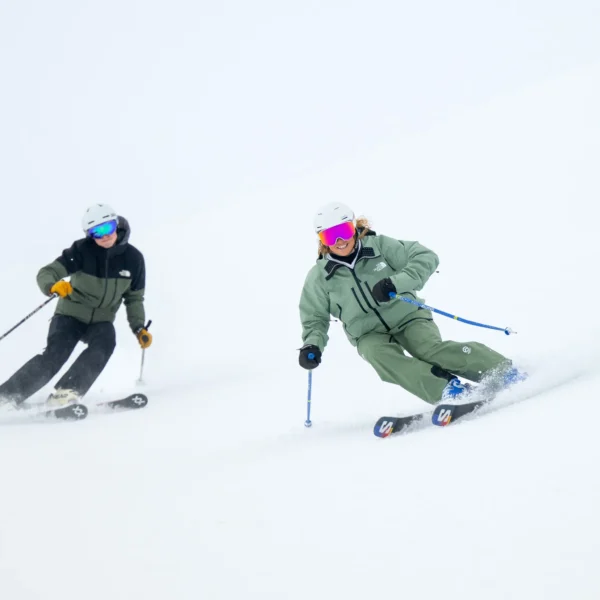 A coach being followed by a student as they make turns down a snowy piste.