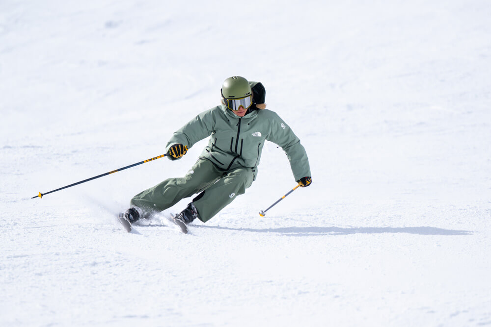 Skier in green jacket carving a sharp turn on groomed slope