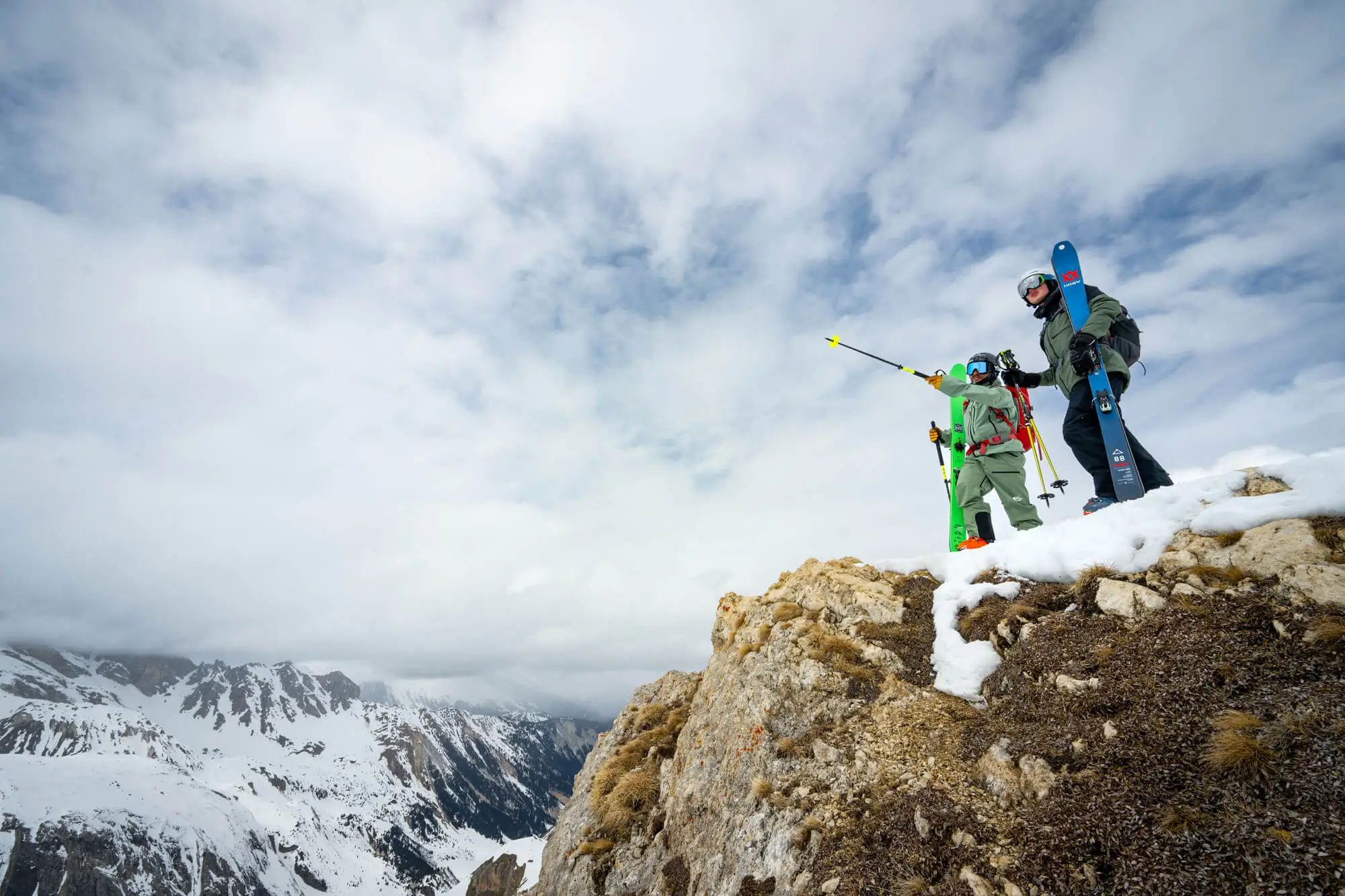 Group of skiers with gear standing on snowy mountain ridge overlooking alpine peaks