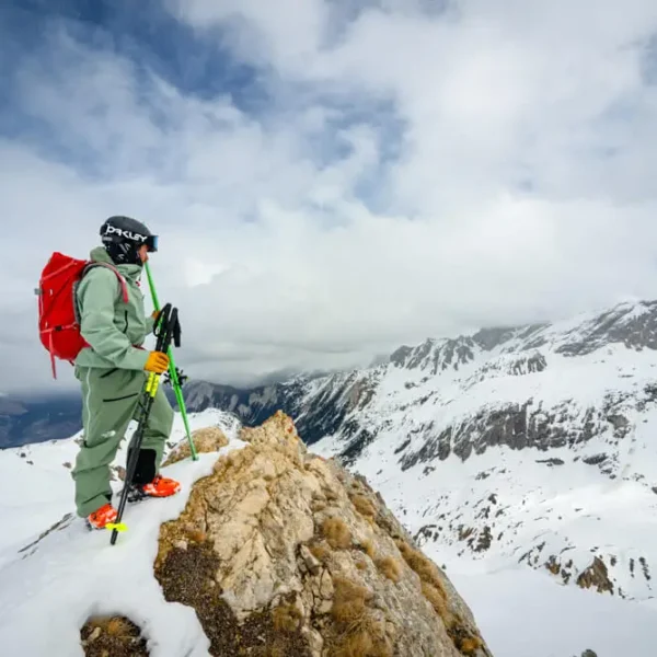 Skier with red backpack standing on mountain peak holding skis and poles