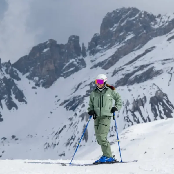 Female skier smiling on snow slope with dramatic alpine peaks behind