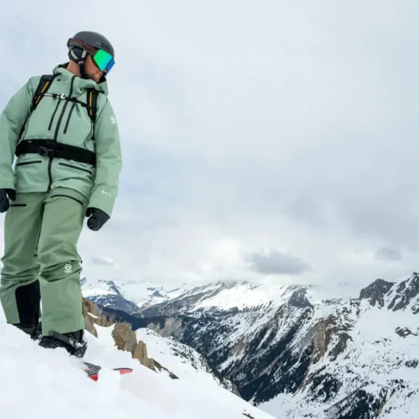 Snowboarder standing on mountain slope with panoramic view of snowy Alps
