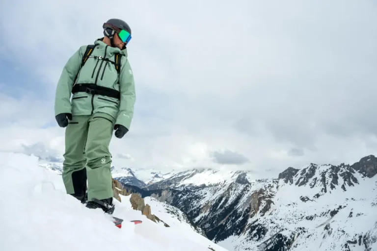 Snowboarder standing on mountain slope with panoramic view of snowy Alps