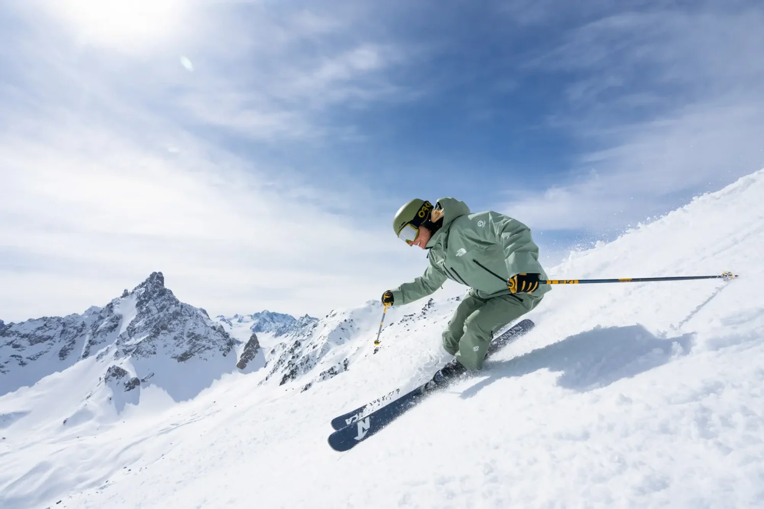 Skier carving a steep powder slope in the Alps under blue sky