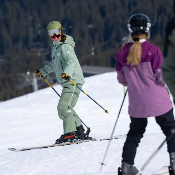 a Ski instructor in Verbier delivering a group ski lesson. The instructor is looking over their left shoulder towards the pupils in the ski lesson. The background is a tree lined mountain back drop.