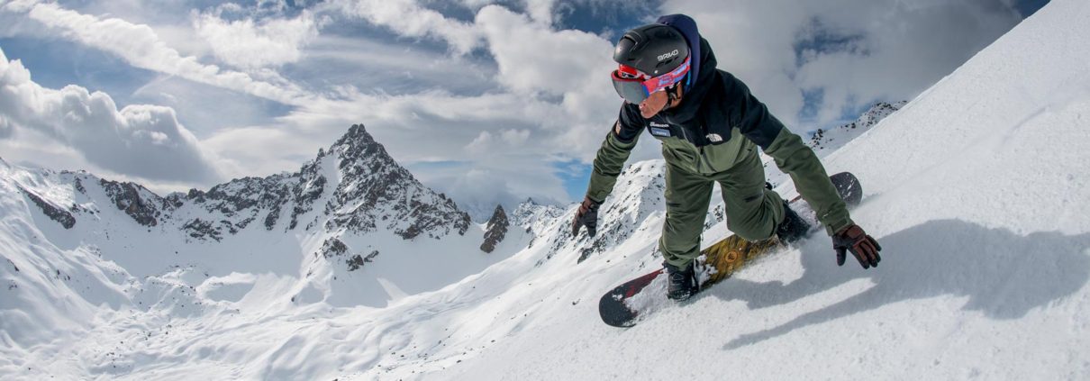 A snowboard instructor making a turn with an impressive mountain backdrop